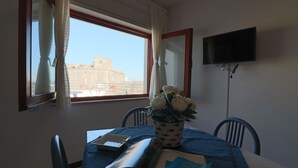 Una habitación con una mesa de comedor, sillas, una planta en maceta, un libro y un televisor montado en la pared.