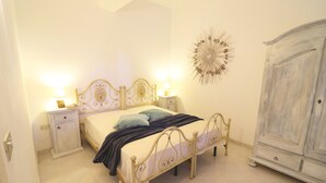 A bedroom with a bed, bedside tables, a wardrobe, and a decorative wall piece. - Casa Primus Torre Santo Stefano in Otranto (Otranto)