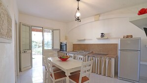 A kitchen with a dining table, chairs, a refrigerator, a sink, and a window with a view of greenery. - Casa Primus Torre Santo Stefano in Otranto (Otranto)