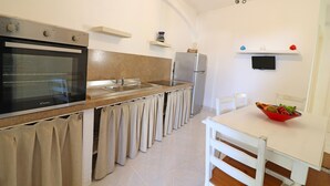 A kitchen with a built-in oven, a refrigerator, a sink, and a dining table with chairs. - Casa Primus Torre Santo Stefano in Otranto (Otranto)
