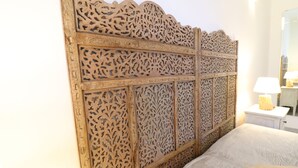Un lit avec une tête de lit en bois ornée de sculptures complexes, une table de chevet avec une lampe et un miroir accroché au mur.