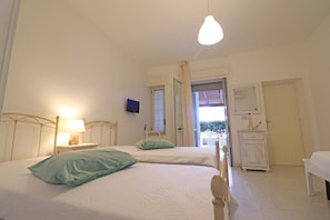 Une chambre avec deux lits, une table de chevet avec une lampe, un téléviseur fixé au mur et une porte donnant sur un espace extérieur.
