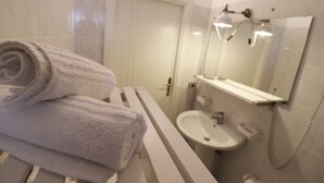 Un baño con un lavamanos blanco, un espejo y un perchero para toallas.