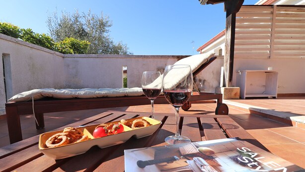 Una mesa de madera con una revista, dos copas de vino, un bol de comida y un banco.