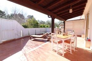 Un patio exterior con una mesa y sillas, una tumbona y una zona cubierta con una lámpara colgante.