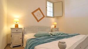 Un dormitorio con una cama, dos mesitas de noche con lámparas, una ventana y un cuadro en la pared.