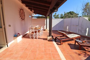 Un patio techado con una mesa, sillas, un sillón de descanso y piso de baldosas.