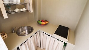 Cocina compacta con un lavabo, escurreplatos, un tazón de fruta y un pequeño canasto de madera.