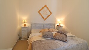 Une chambre à coucher comprenant un lit, deux tables de chevet avec des lampes, un tableau accroché au mur et un petit meuble.