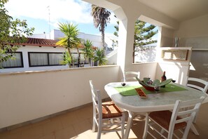 Un balcon avec une table et des chaises, un tapis vert, une bouteille et un verre de vin rouge.