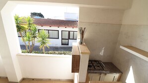 Une cuisine compacte équipée d’une cuisinière à gaz, d’un petit plan de travail et offrant une vue sur un bâtiment doté d’un toit en tuiles et de palmiers.
