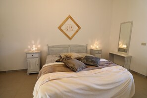 A bedroom with a bed, two bedside tables, a nightstand, a wall-mounted mirror, and a framed picture. - Casa Black Magic Torre Santo Stefano in Otranto 6 places (Otranto)