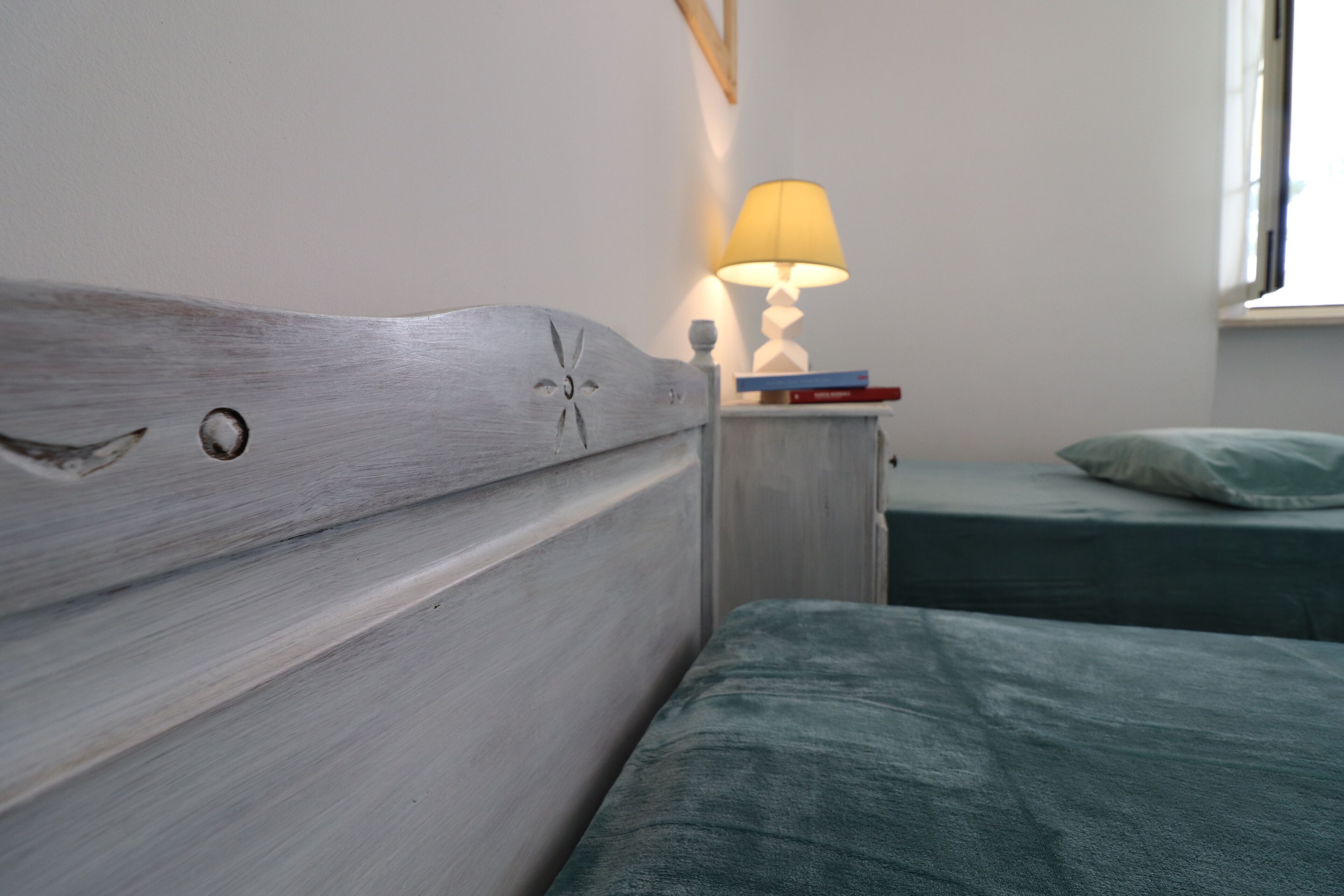 Un dormitorio con cabecera de madera, una mesita de noche con lámpara y dos camas con ropa de cama verde.