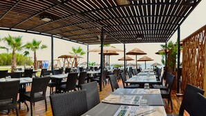 An outdoor restaurant with tables and chairs, umbrellas, and a view of the ocean.