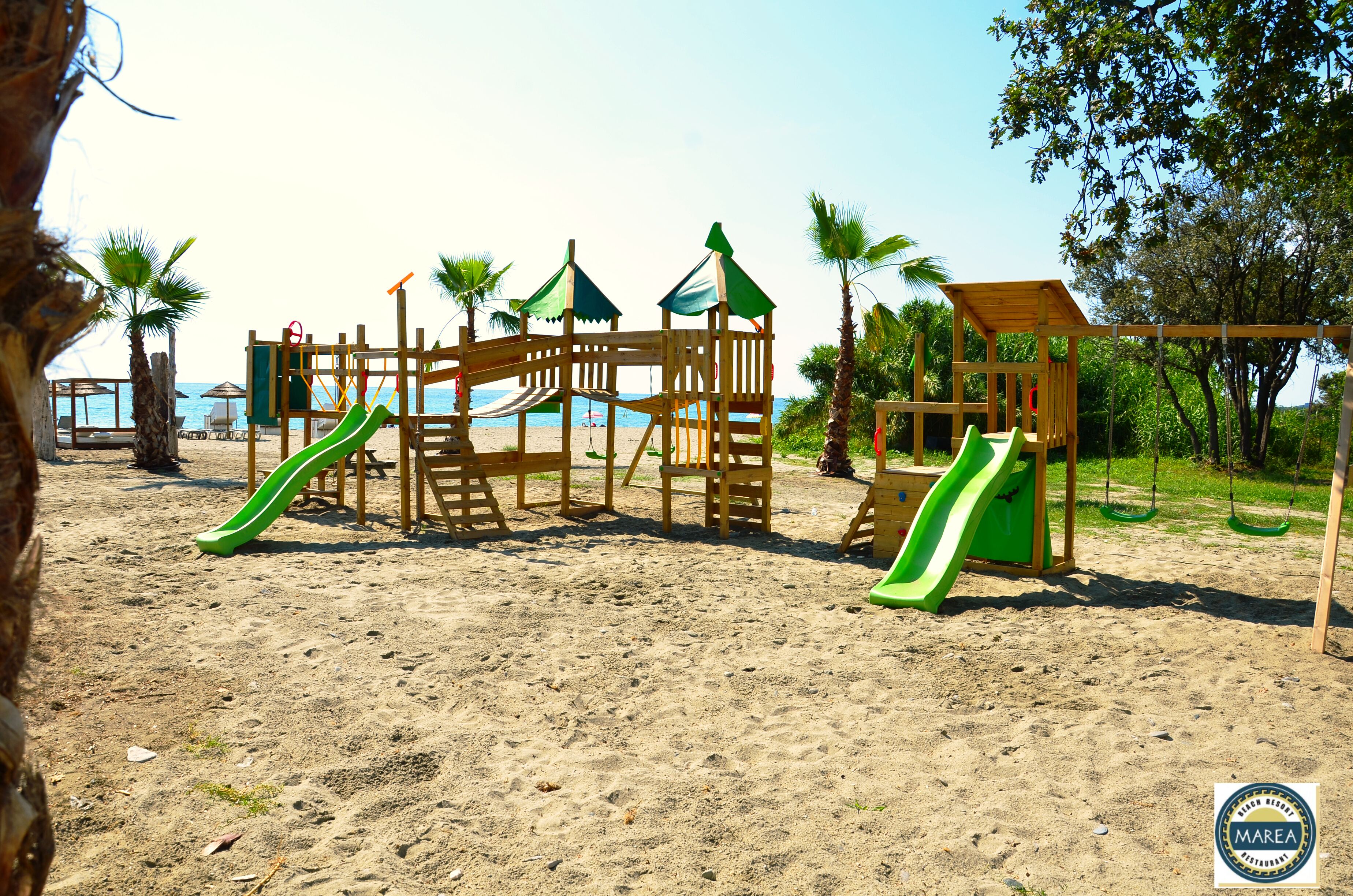 A wooden playground with slides and climbing structures on a sandy beach.