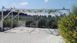 A gated entrance with a white pergola structure, gravel ground, and surrounding greenery. - "lu Ientu" house in Otranto, Baia dei Turchi area 1 (Otranto)