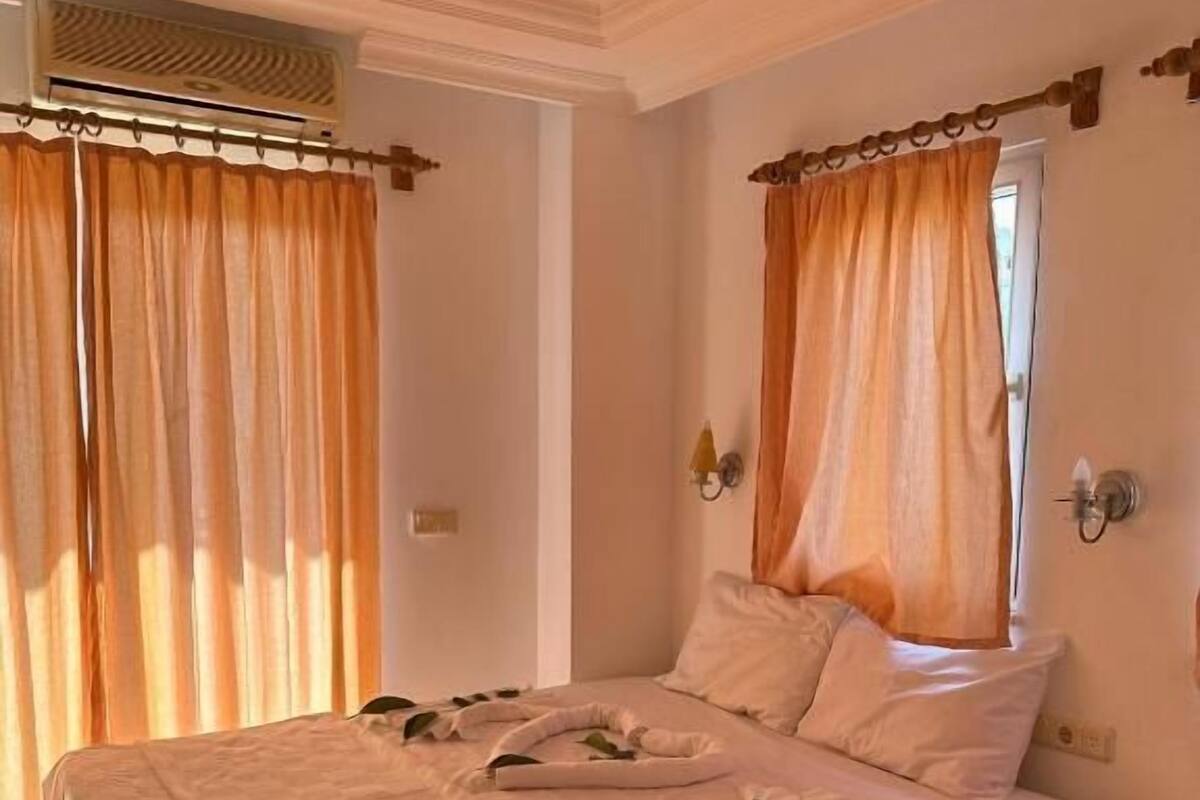 A neatly made bed with white linens, a checkered floor, and a wooden nightstand with a drawer.