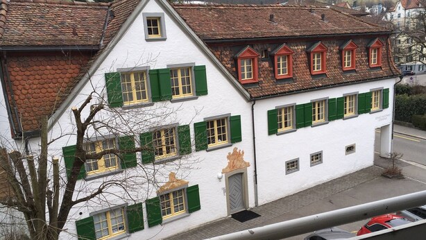 A white building with green shutters and a red-tiled roof. - 2 rooms with balcony, central, quiet location (St. Gallen)