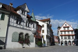 Une rue historique européenne, bordée de bâtiments à l’architecture traditionnelle, dont l’un est surmonté d’un toit végétalisé et l’autre d’un toit rouge.