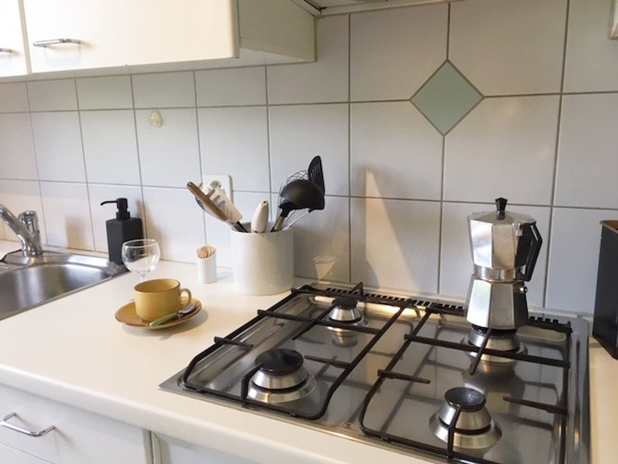 Et køkken med gaskomfur, kaffemaskine, en kop kaffe og en krydderiholder.