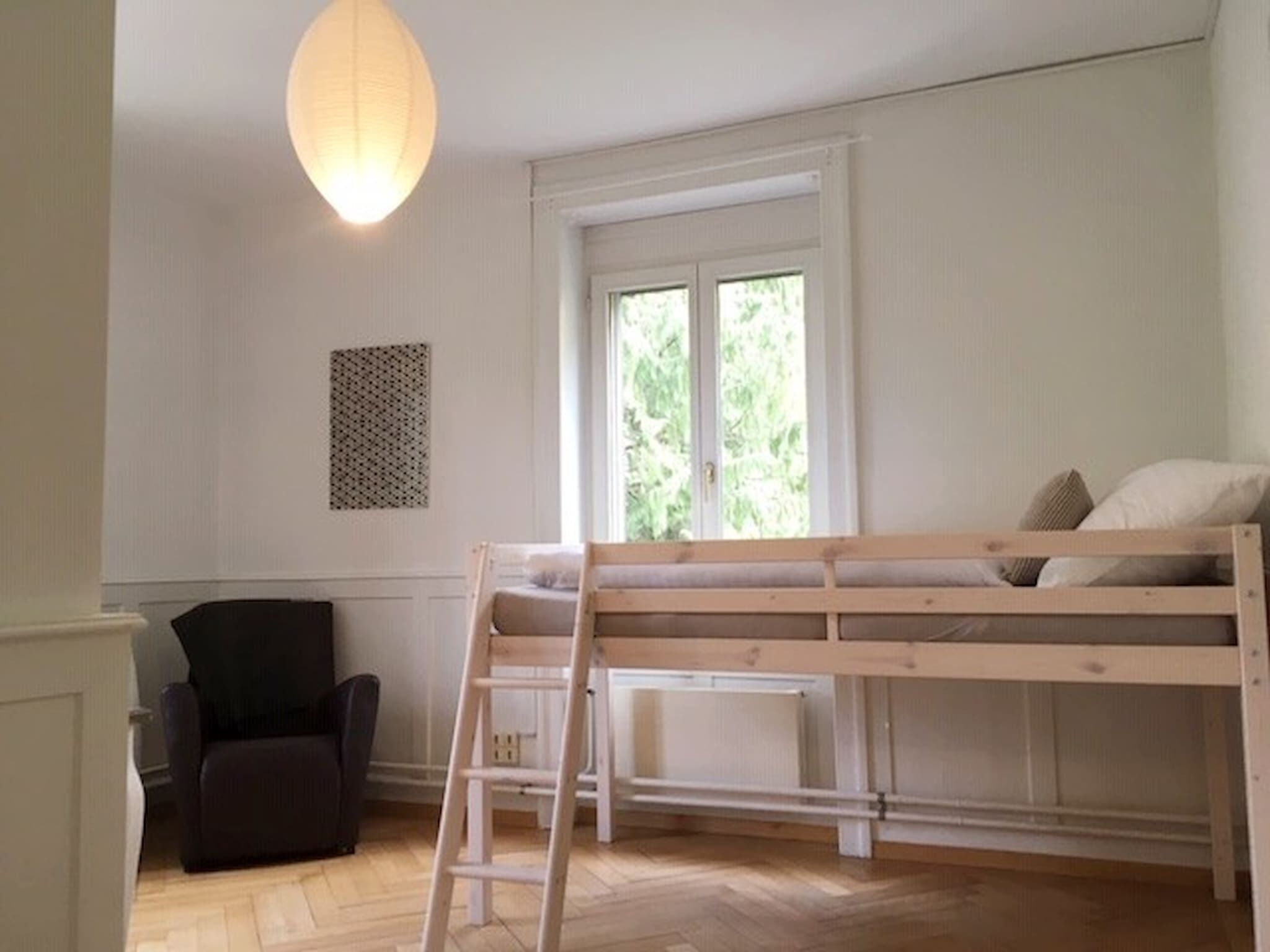 Une chambre avec un lit superposé, un bureau, une chaise et une fenêtre donnant sur un paysage verdoyant.