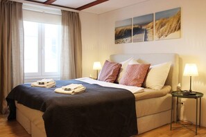 Un lit bien fait, recouvert d’une couvre-lit à motifs sombres, avec deux oreillers et des serviettes pliées posées sur le côté. Deux lampes murales sont fixées de chaque côté du lit.