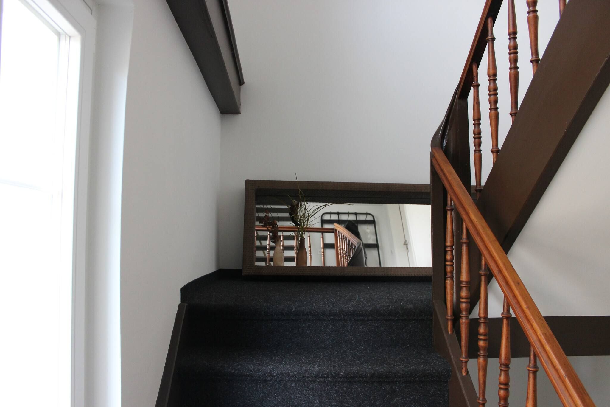 Un escalier avec une rampe en bois et un palier recouvert d’une moquette sombre.