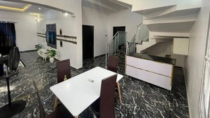 A modern hotel room with a marble floor, a dining area with a white table and chairs, a staircase, and a TV mounted on the wall. - Immaculate 4-bed Detached Duplex in Lekki Chevron (Lekki)