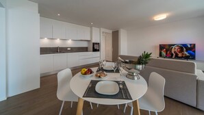 A modern kitchen with white cabinets, a dining table with chairs, and a TV mounted on the wall. - Vacation Rental City 10 in Massagno (Massagno)