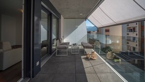A modern balcony with a glass railing, a sofa, two chairs, a small table, and a wicker basket. - Vacation Rental City 10 in Massagno (Massagno)