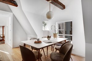 A dining area with a white table, brown chairs, a hanging light fixture, and a window with a view. - Regent 6- Cozy 1-Bdr Apt with Terrace in the Centre of Copenhagen (København)