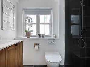 Een moderne badkamer met een wit toilet, een raam met planten, een douche en een handdoekrek.