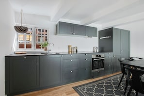 A modern kitchen with dark cabinetry, a built-in oven, and a dining area with a table and chairs. - Regent 2- Endearing 1-Bdr Apt in Centre of Copenhagen (København)
