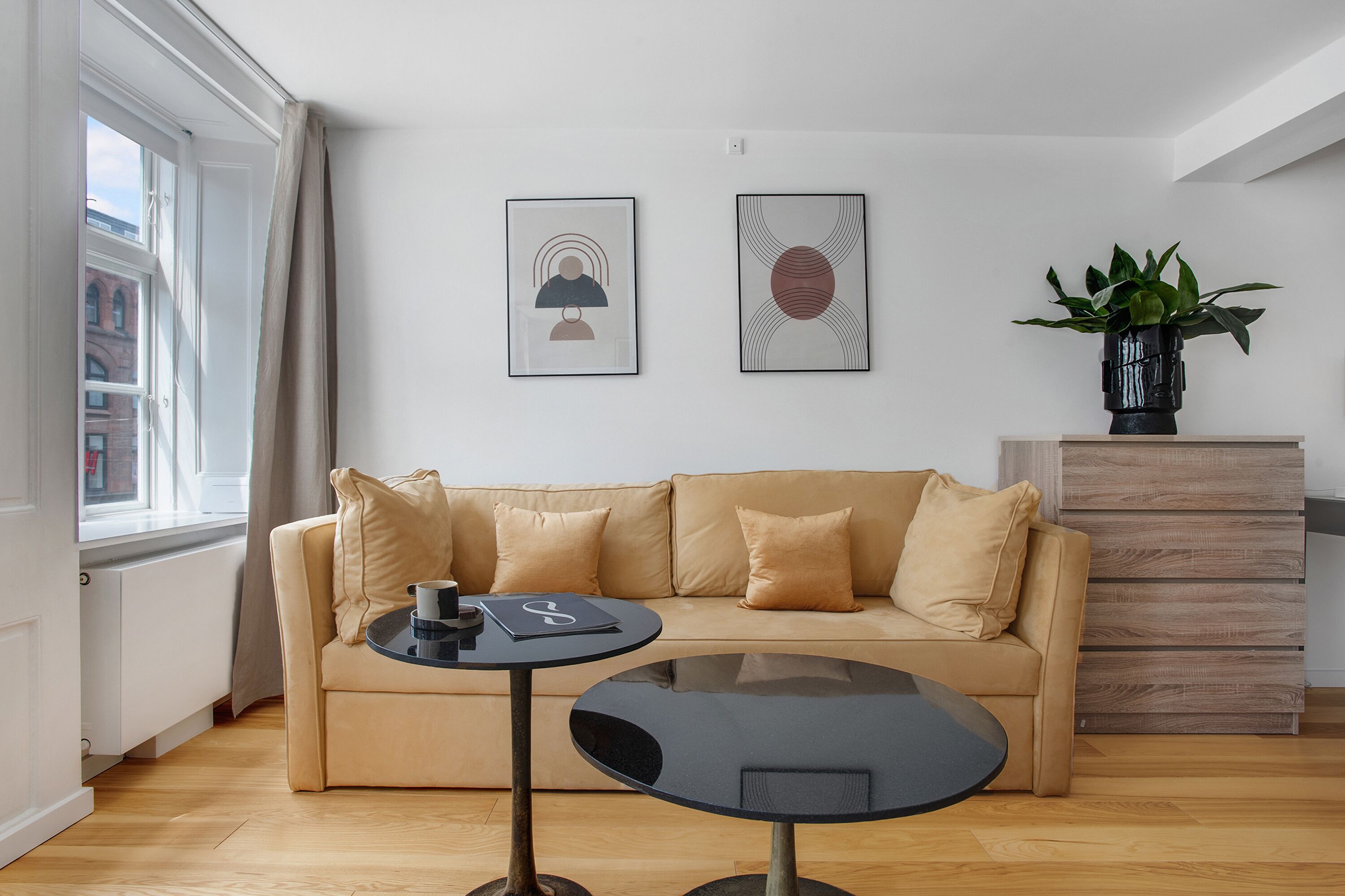 Ett modernt vardagsrum med en beige soffa, ett runt svart soffbord och två inramade konstverk på väggen.