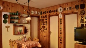 Ein Zimmer mit Holzwänden, ein Esstisch für zwei Personen gedeckt, einem Fernseher und verschiedenen dekorativen Tellern und Objekten an den Wänden.
