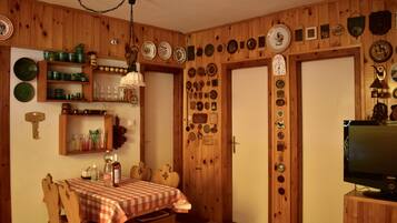 Une pièce aux murs lambrissés, avec une table à manger dressée pour deux personnes, un téléviseur, ainsi que divers objets décoratifs et assiettes ornant les murs.
