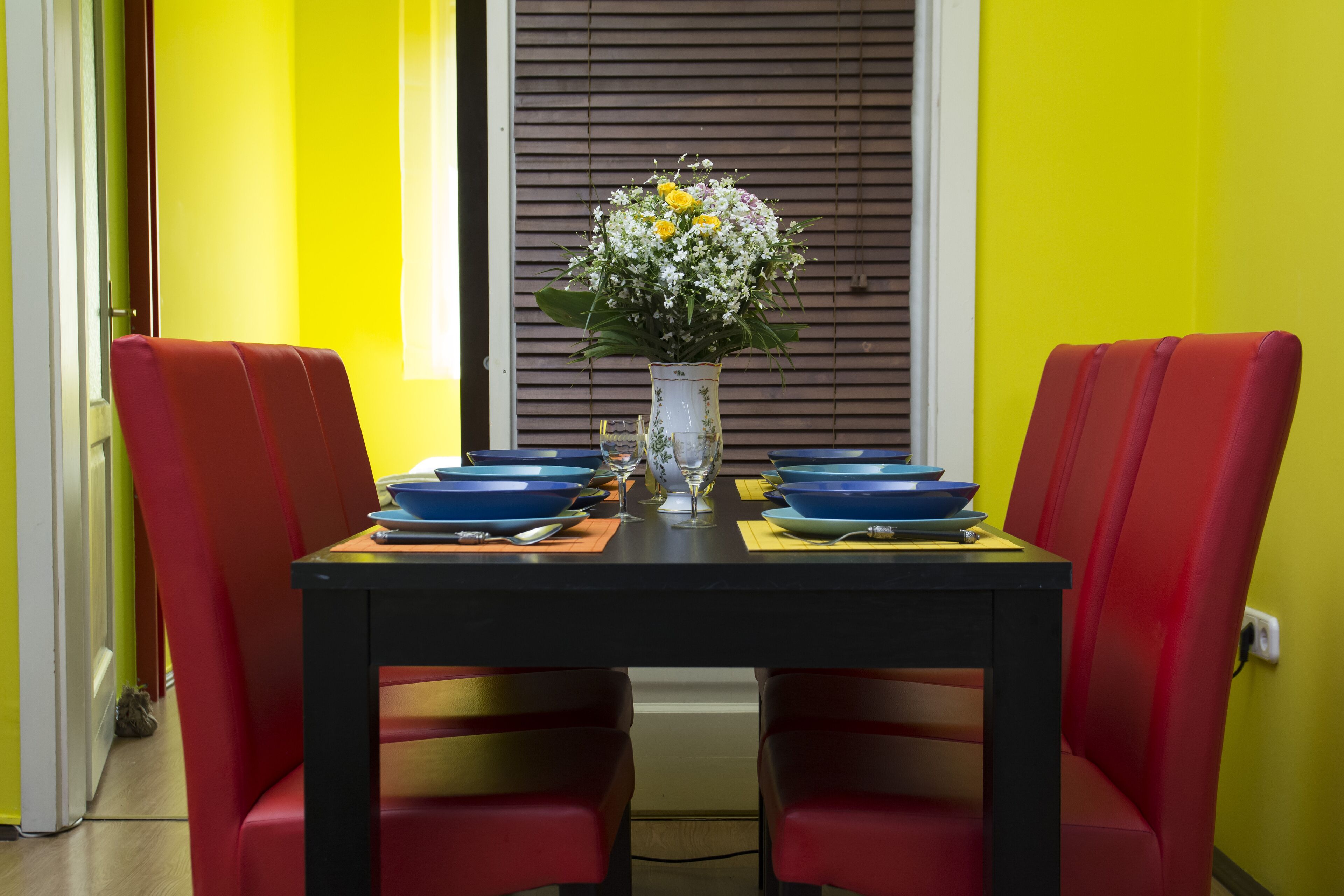 A dining table with red chairs, a vase with flowers, and blue plates.