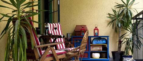 A patio with wicker chairs, a striped tablecloth, and potted plants.