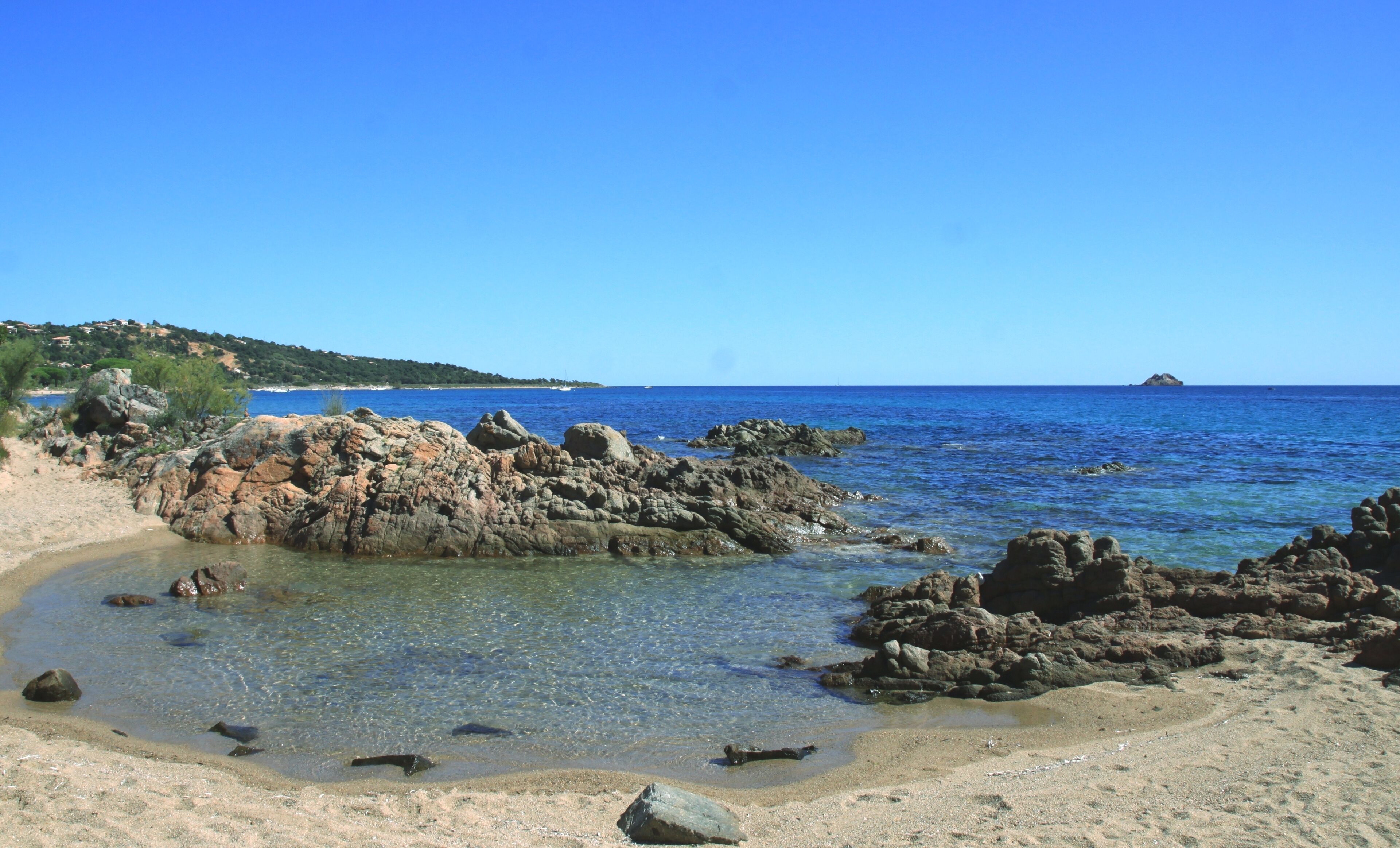 Ein felsiger Strand mit klarem Wasser und einer fernen Insel.