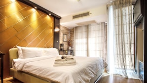 A hotel room with a large bed, a wooden headboard, a bedside table, a TV, and a window with curtains.