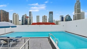 A rooftop pool with a city skyline view, a red-roofed building in the background, and a blue umbrella. - 3A - Short-Term Rental Allowed - Downtown Bkk Serviced Apartment (Krung Thep Maha Nakhon)