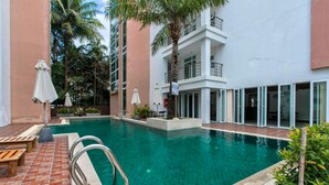 A swimming pool with a brick deck, lounge chairs, and umbrellas. - 6-35 - 3 Bdr Condo with Balcony and shared Pool (Tambon Patong)