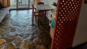 A room with a stone floor, wooden ceiling beams, a dining table, and a view through a glass door. - Apartment with Pool and Panorama View (Koumeika)