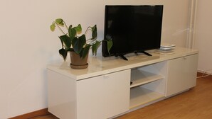 Eine weiße Unterhaltungseinrichtung mit einem Flachbildfernseher, einer Topfpflanze und einem kleinen weißen Gerät darauf.