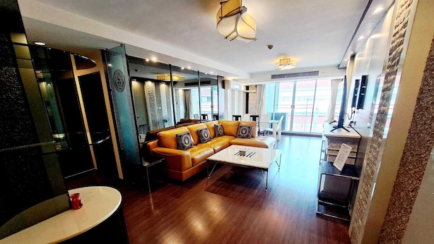 Una sala de estar moderna con un sofá de cuero, una mesa de centro y un televisor. Hay ventanas amplias y vistas al exterior.