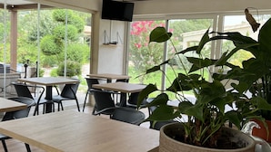 Un espace repas avec des tables et des chaises, une grande plante en pot et un téléviseur fixé au mur.