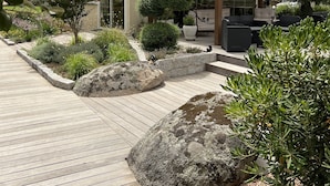 Une terrasse en bois agrémentée d’une pergola, entourée de jardins aménagés et comprenant un espace détente avec des meubles d’extérieur.