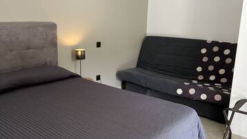 A bedroom with a large bed, a sofa, a wall-mounted lamp, and a painting.