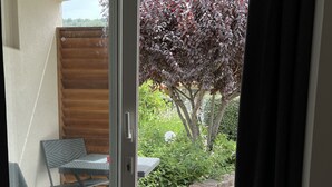 An open sliding glass door leading to an outdoor patio area with a table and chairs, a tree with red leaves, and a stone pathway.