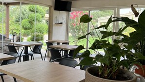 An indoor dining area with tables and chairs, a potted plant, and a television mounted on the wall. - Les Jardins De Santa Giulia - Charmante chambre d'hôte (Porto-Vecchio)